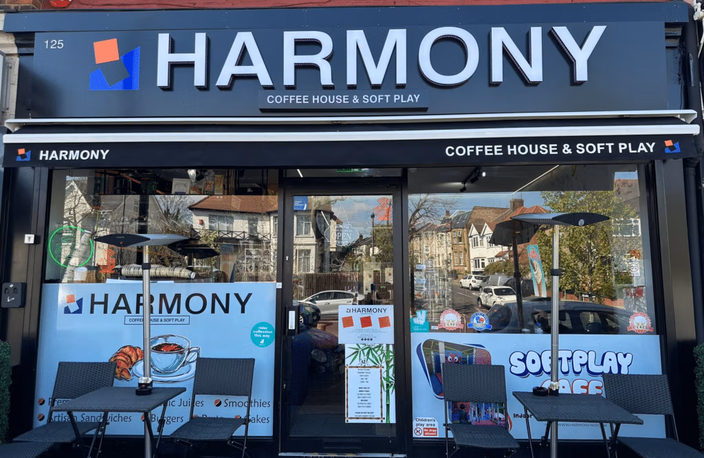 Exterior of Harmony Coffee House and Soft Play café with dark shopfront fascia, branded window graphics advertising food and drinks, and outdoor seating with heaters