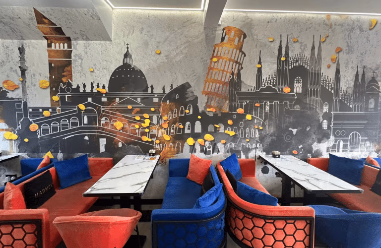 Refurbished café seating area with Italian landmarks mural, red and blue velvet booth seating, marble-effect tables, and hexagonal patterned booth fronts